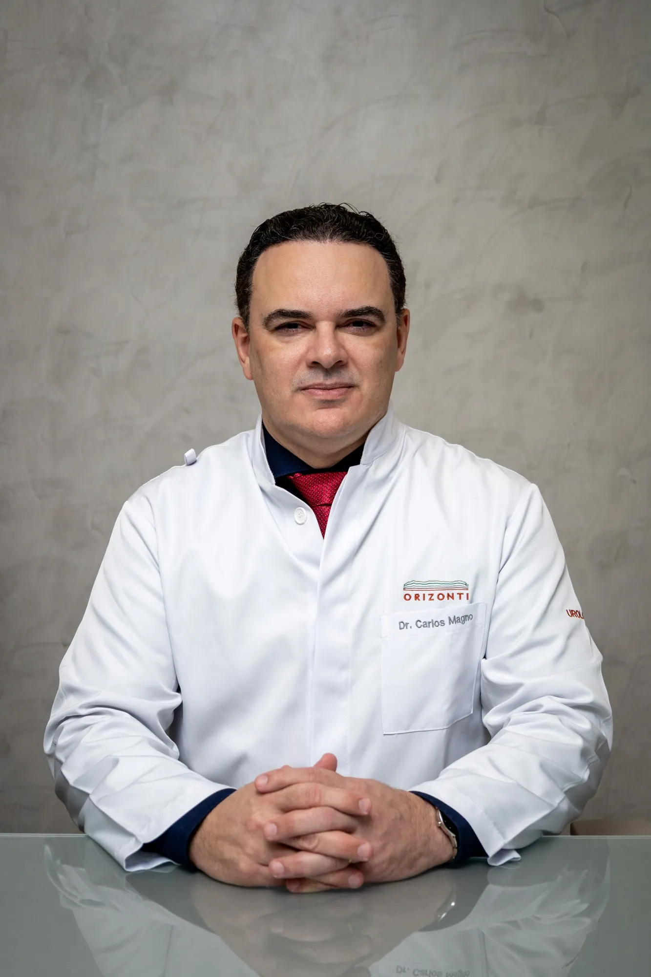 Dr. Carlos Magno sentado à mesa do consultório, de jaleco